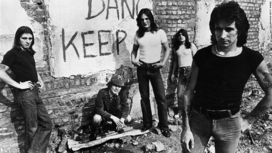 1977:  Promotional portrait of Australian hard-rock group AC/DC standing in front of a graffiti-covered brick wall, (L-R:) drummer Phillip Rudd, guitarist Angus Young, bassist Mark Evans, guitarist Malcolm Young, and lead singer Bon Scott.  Angus Young crouches, wearing his trademark schoolboy uniform.  (Photo by Hulton Archive/Getty Images)