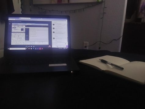 Laptop and notebook placed side by side on a bed.