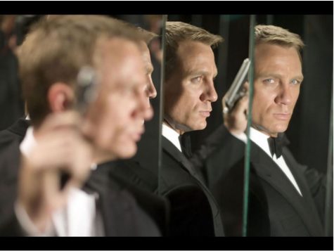 A picture of a man in a Black suite holding a gun standing in front of mirrors giving the allusion that there are three of him.