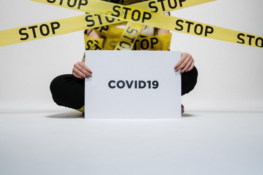 Someone sitting on the floor with a sign that says Covid-19 and caution tape around them with the word stop.
