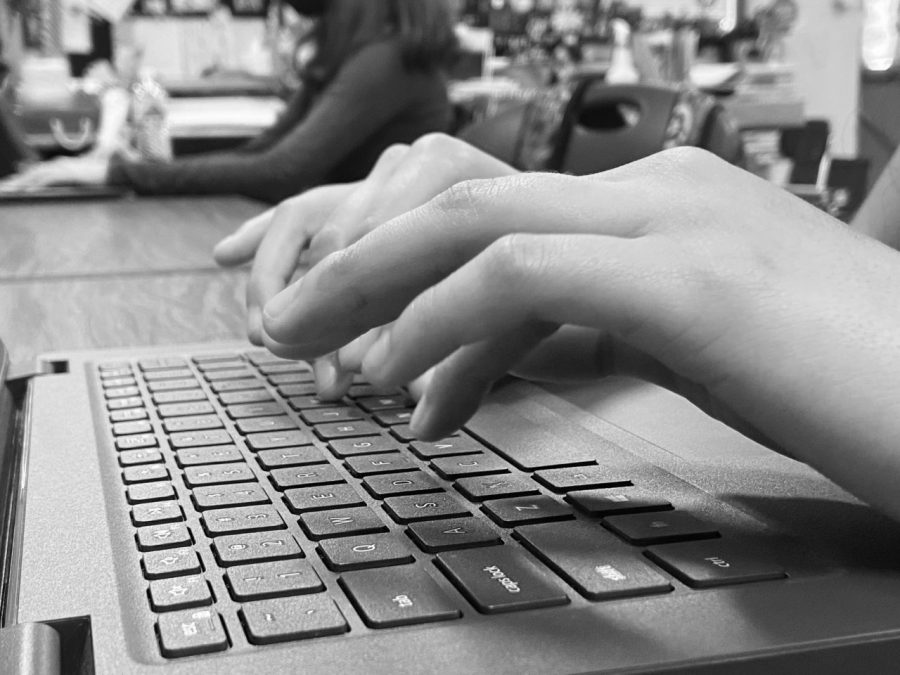 A black and white image of someones hands typing on a keyboard.