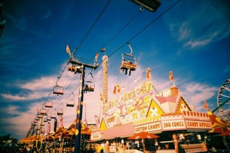 It is a picture of a seated zipline from the state fair with carnival games lined up in the background.