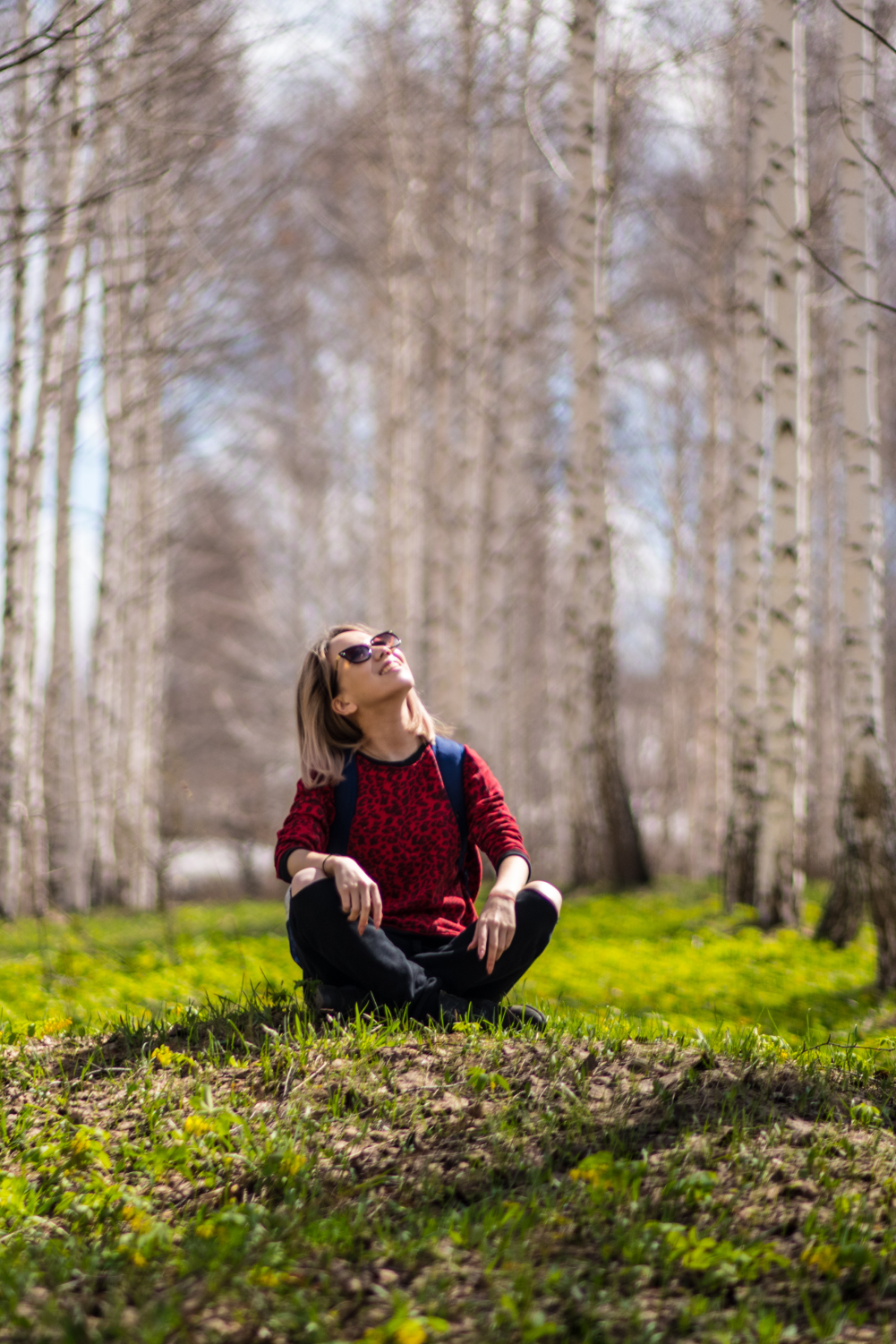 Girl sitting in the woods while looking towards the sunny sky with sunglassses