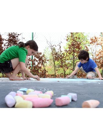 Children using colorful chalk to draw different creative images on the sidewalk.
