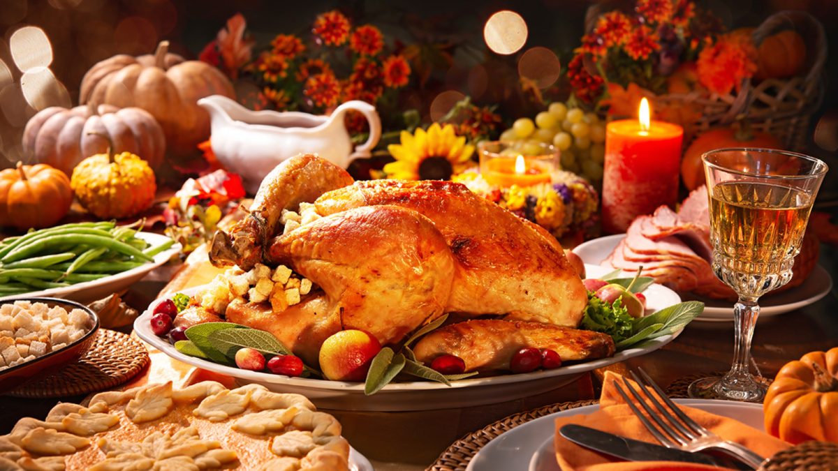 Thanksgiving dinner. Roasted turkey garnished with cranberries on a rustic style table decoraded with pumpkins, vegetables, pie, flowers and candles; Shutterstock ID 1192275073